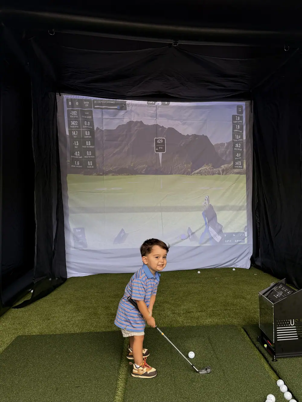 A young guest taking a swing inside the bay with the course on screen